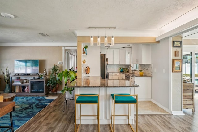 kitchen with decorative light fixtures, white cabinetry, backsplash, a kitchen bar, and kitchen peninsula