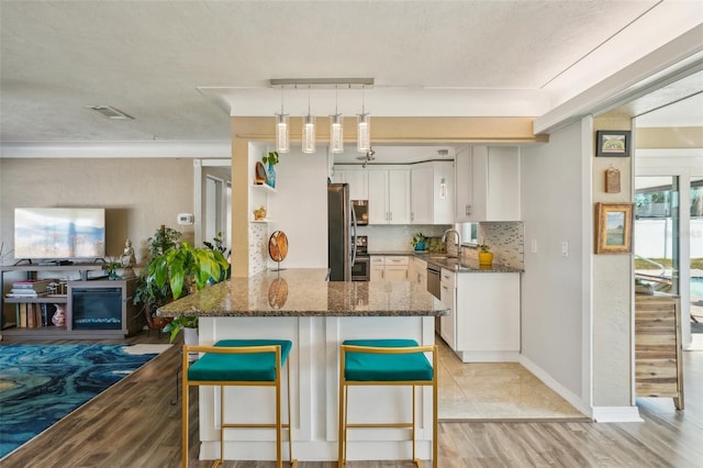 kitchen featuring a breakfast bar area, white cabinetry, kitchen peninsula, dark stone counters, and backsplash