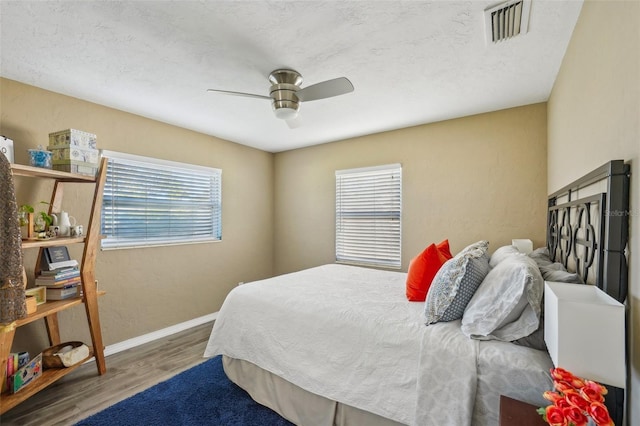 bedroom featuring multiple windows, hardwood / wood-style flooring, a textured ceiling, and ceiling fan