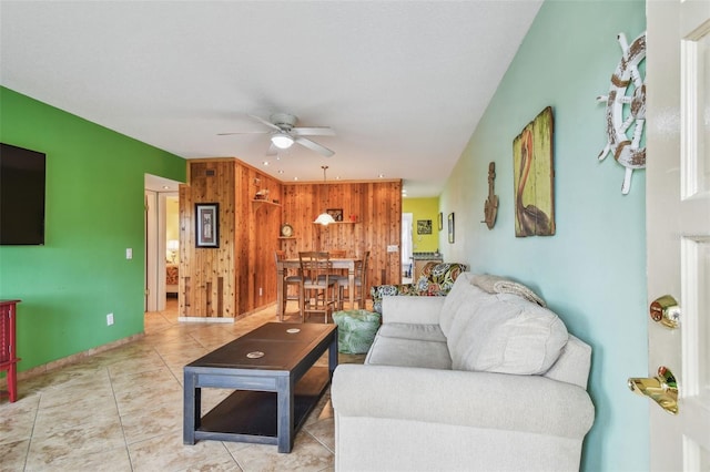 living room with light tile patterned floors, ceiling fan, and wood walls