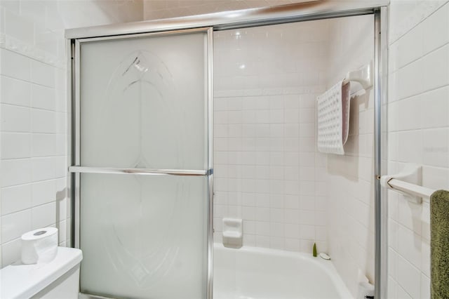 bathroom with enclosed tub / shower combo, toilet, and tile walls
