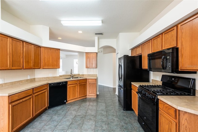 kitchen with brown cabinetry, light countertops, arched walkways, black appliances, and a sink