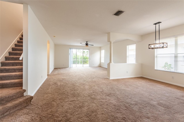 unfurnished room with visible vents, light colored carpet, stairs, ornate columns, and a ceiling fan