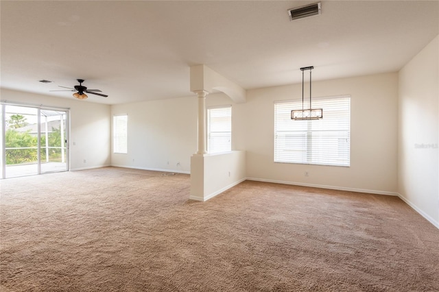 empty room featuring visible vents, baseboards, light colored carpet, ceiling fan, and ornate columns