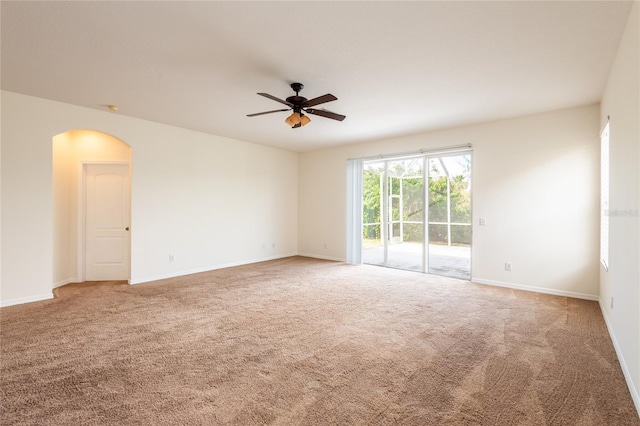 carpeted empty room with baseboards, arched walkways, and ceiling fan