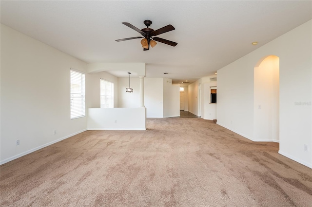 carpeted empty room with baseboards, arched walkways, and ceiling fan