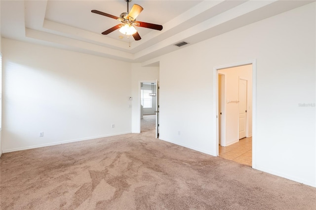 carpeted empty room with baseboards, visible vents, a ceiling fan, and a tray ceiling