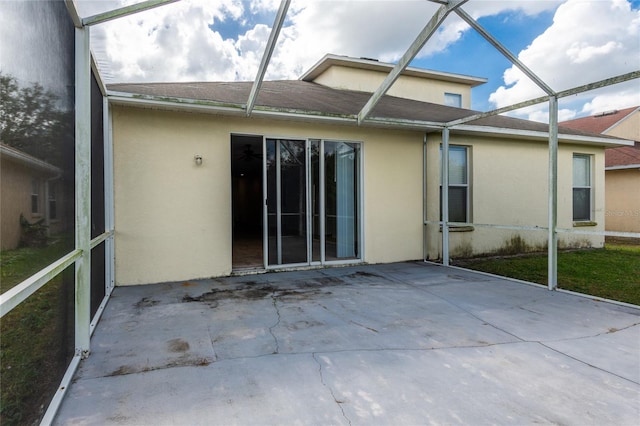 rear view of house featuring glass enclosure, a patio, and stucco siding