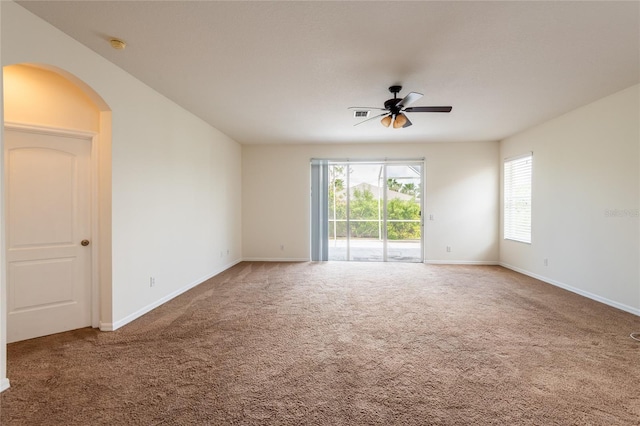 carpeted spare room featuring visible vents, arched walkways, baseboards, and ceiling fan