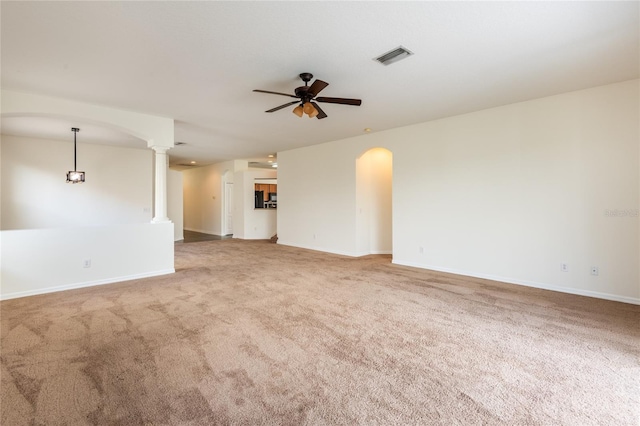 carpeted empty room with visible vents, baseboards, arched walkways, a ceiling fan, and ornate columns