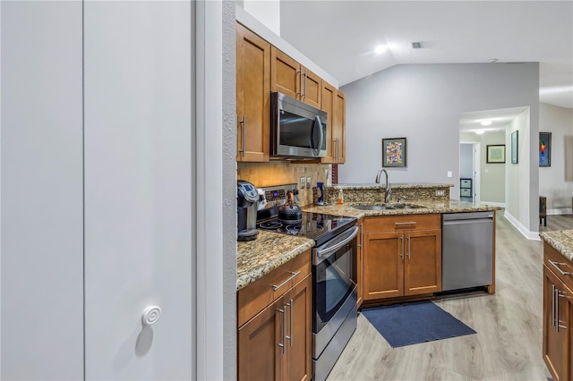 kitchen with lofted ceiling, sink, light stone countertops, and appliances with stainless steel finishes