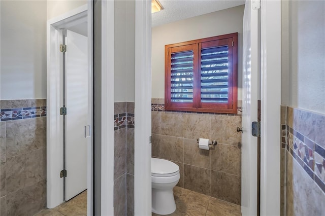 bathroom with tile walls, tile patterned floors, a textured ceiling, and toilet