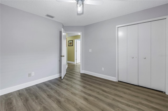 unfurnished bedroom with ceiling fan, a closet, dark hardwood / wood-style flooring, and a textured ceiling