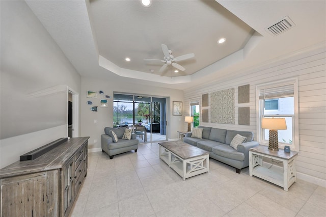 living room featuring ceiling fan, a tray ceiling, and light tile patterned floors