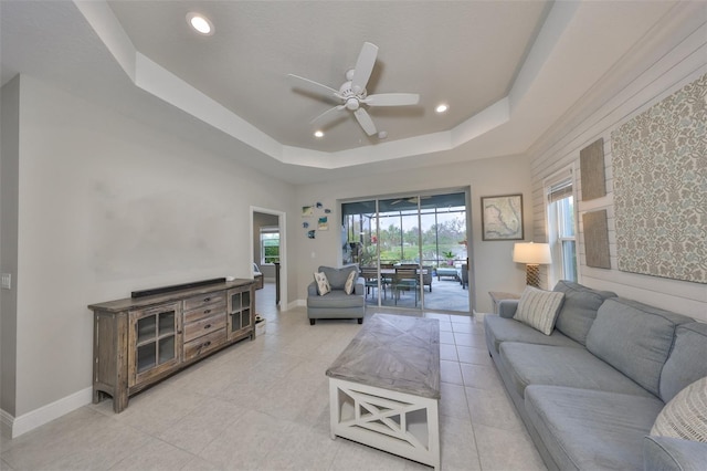 living room with light tile patterned floors, a raised ceiling, and ceiling fan