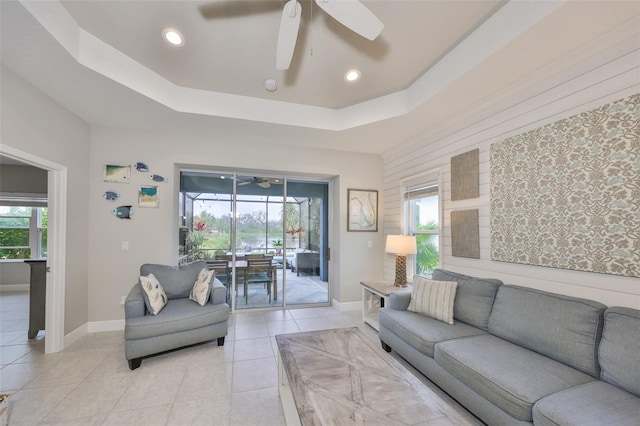 living area featuring ceiling fan, plenty of natural light, a raised ceiling, and light tile patterned flooring