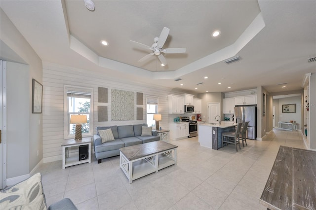 living room featuring a raised ceiling, sink, light tile patterned floors, and ceiling fan