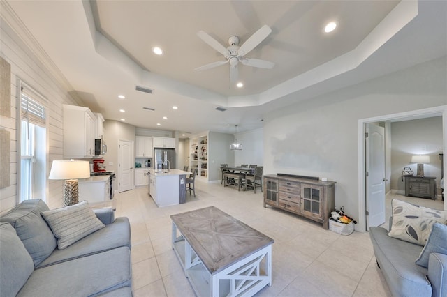 living room featuring light tile patterned flooring, ceiling fan, and a raised ceiling