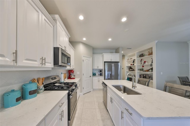 kitchen with an island with sink, light stone countertops, stainless steel appliances, white cabinetry, and a sink