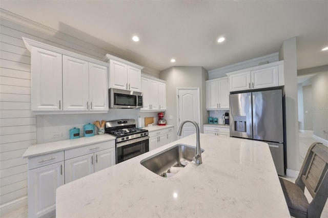 kitchen with stainless steel appliances, light stone counters, a sink, and white cabinets