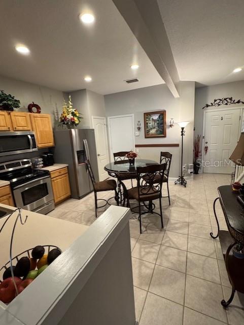 kitchen with light tile patterned floors, beam ceiling, and stainless steel appliances