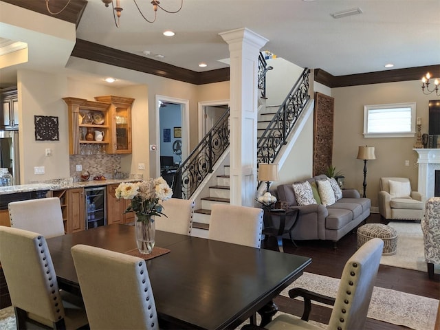 dining room featuring decorative columns, beverage cooler, ornamental molding, dark wood-type flooring, and an inviting chandelier