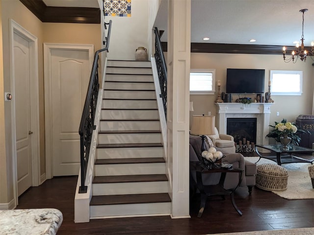 stairway with crown molding, wood-type flooring, a premium fireplace, and a chandelier