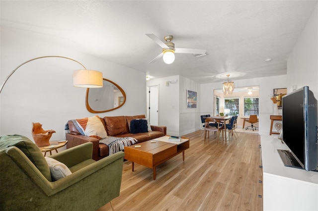 living area featuring light wood-type flooring, a textured ceiling, baseboards, and a ceiling fan