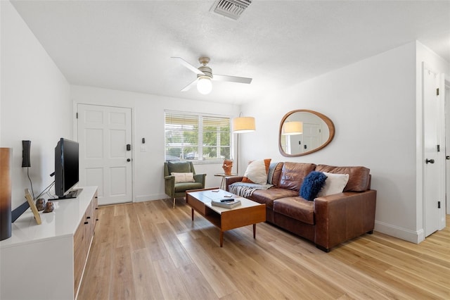 living room featuring a textured ceiling, visible vents, baseboards, a ceiling fan, and light wood finished floors