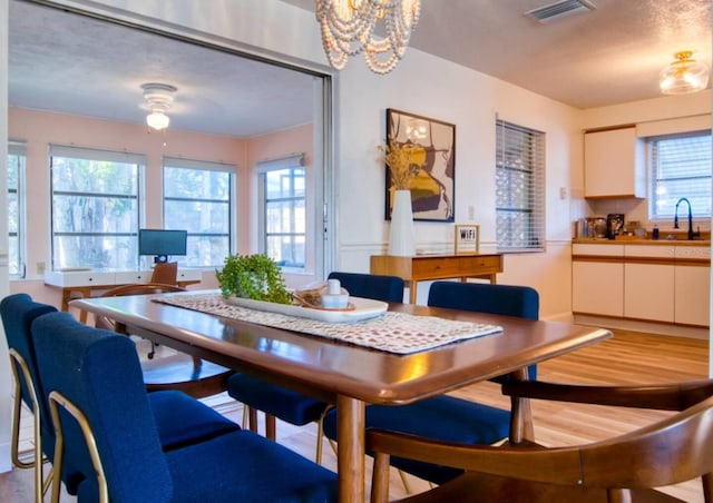 dining area with light wood-style floors, visible vents, and ceiling fan with notable chandelier