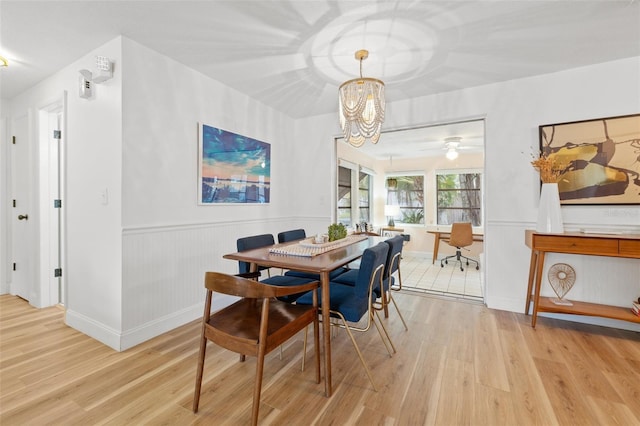 dining area featuring wainscoting, light wood-style flooring, and a notable chandelier