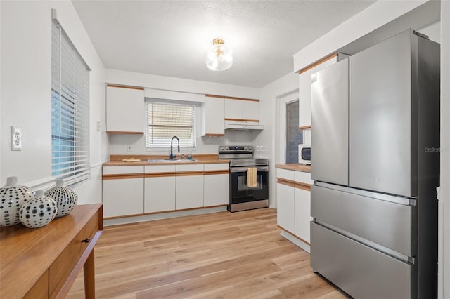 kitchen with white cabinets, light wood-style flooring, stainless steel appliances, under cabinet range hood, and a sink