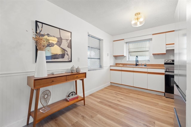 kitchen featuring light wood finished floors, white cabinets, stainless steel electric stove, light countertops, and a sink