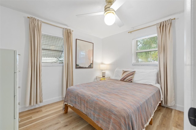 bedroom featuring light wood-style floors, freestanding refrigerator, ceiling fan, and baseboards