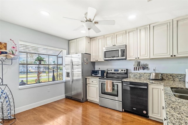 kitchen with light wood-style flooring, appliances with stainless steel finishes, a ceiling fan, light stone countertops, and baseboards