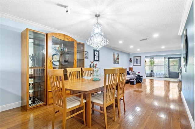 dining room with a textured ceiling, ornamental molding, wood finished floors, and baseboards