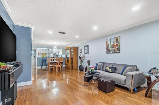 living area featuring visible vents, ornamental molding, a textured ceiling, wood finished floors, and baseboards