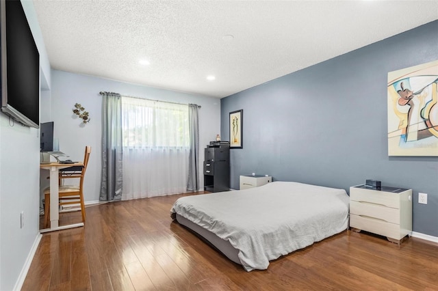 bedroom featuring a textured ceiling, baseboards, and wood finished floors