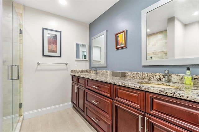 full bathroom featuring double vanity, a shower stall, baseboards, and a sink