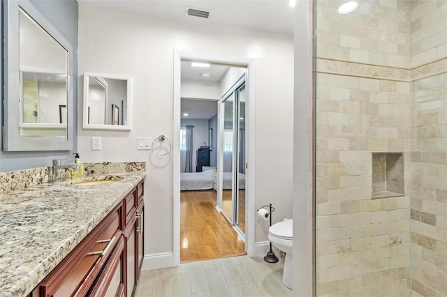 ensuite bathroom with connected bathroom, toilet, wood finished floors, vanity, and visible vents