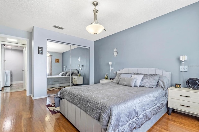 bedroom with washer / dryer, a closet, visible vents, and wood finished floors