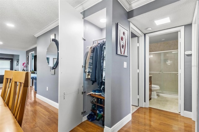 hallway with light wood-style floors, crown molding, and a textured ceiling