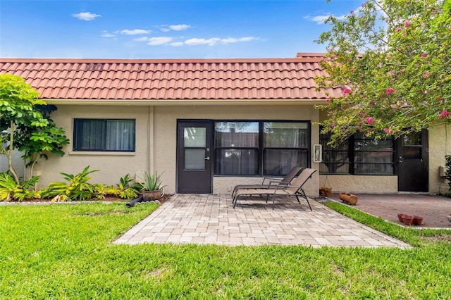 back of house with a patio area, a tiled roof, a lawn, and stucco siding