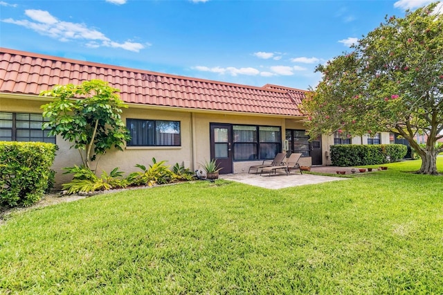 rear view of house with a tile roof, a patio area, a yard, and stucco siding