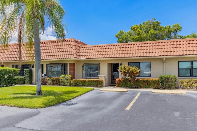 townhome / multi-family property featuring uncovered parking, a front yard, a tiled roof, and stucco siding