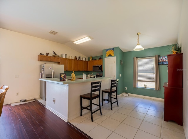 kitchen with light hardwood / wood-style flooring, a breakfast bar, appliances with stainless steel finishes, hanging light fixtures, and vaulted ceiling