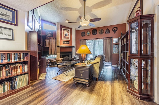 interior space featuring lofted ceiling, wood-type flooring, a textured ceiling, ceiling fan, and a fireplace