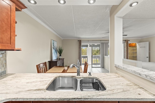 kitchen with sink, crown molding, light stone countertops, and light tile patterned floors