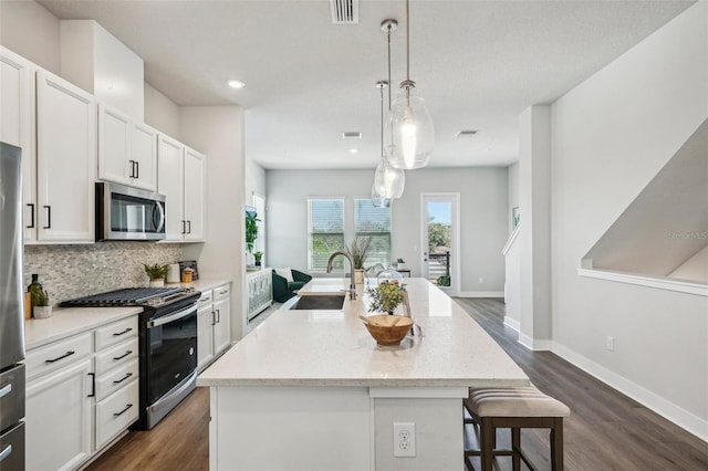 kitchen featuring pendant lighting, sink, appliances with stainless steel finishes, white cabinets, and a center island with sink