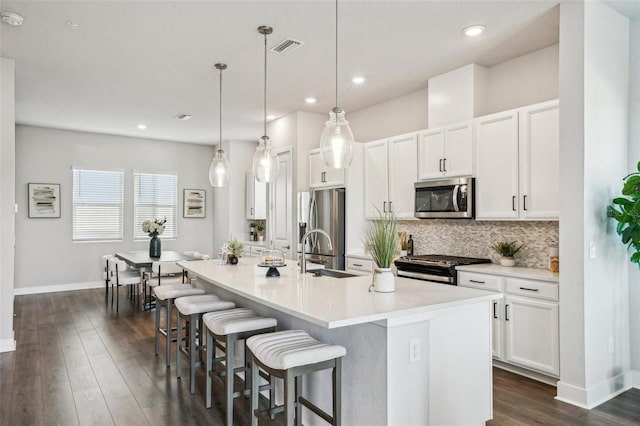 kitchen with stainless steel appliances, white cabinetry, a kitchen island with sink, and pendant lighting